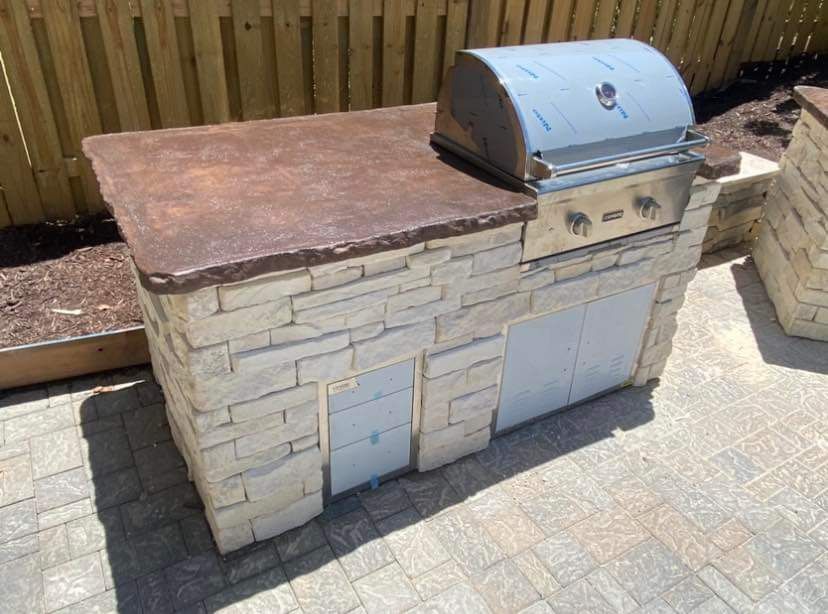 A grill is sitting on top of a stone counter on a patio.