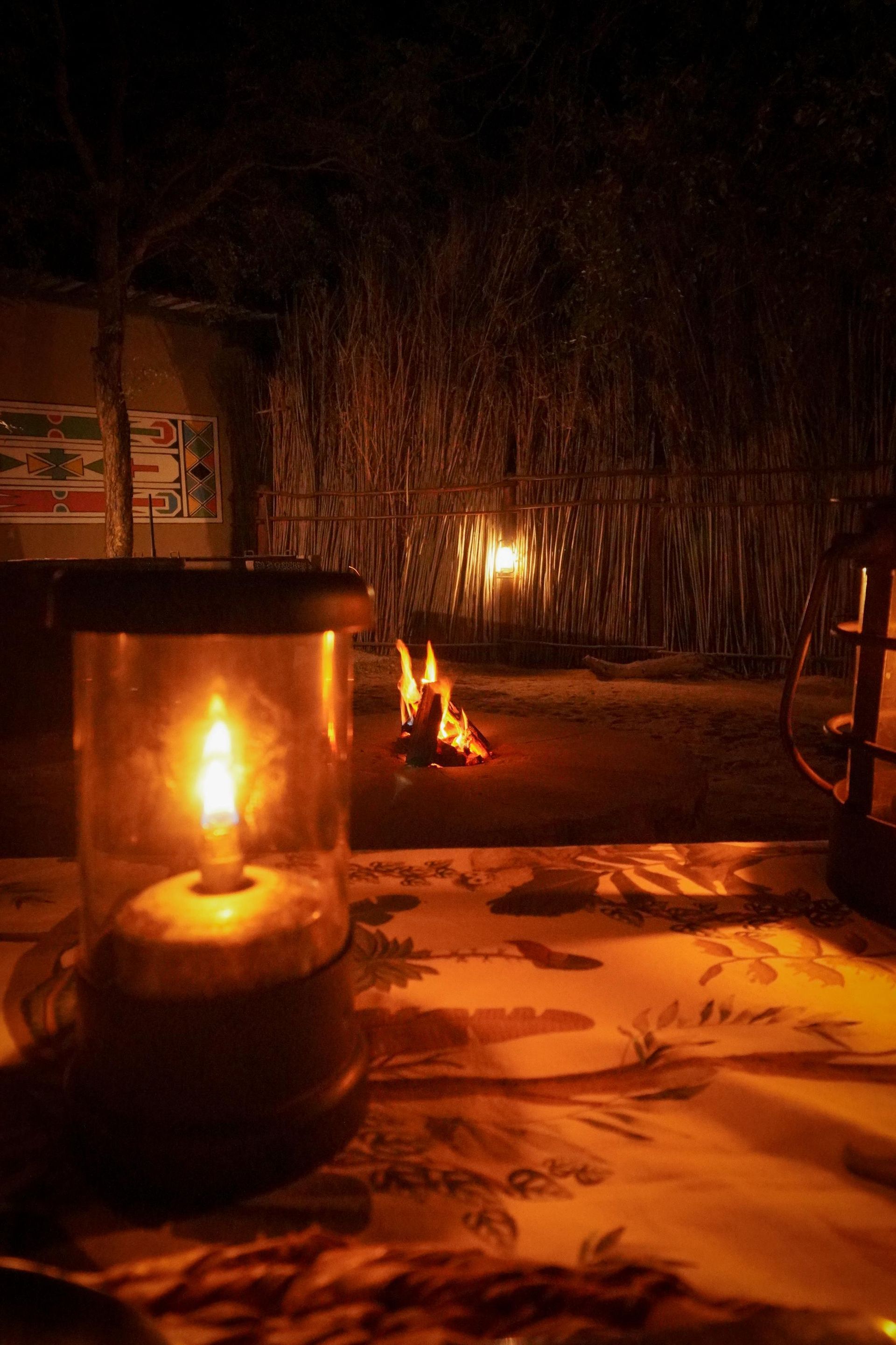 A candle is lit on a table in front of a fire.