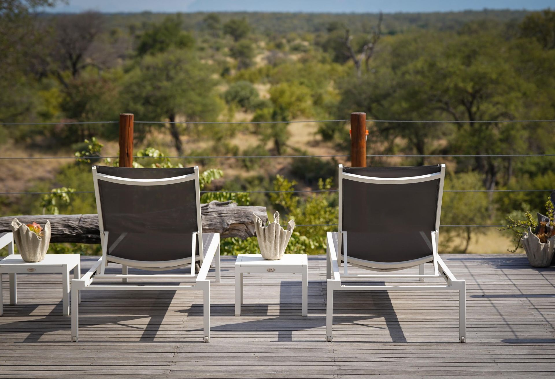 Two lounge chairs are sitting on a wooden deck overlooking a lush green field.