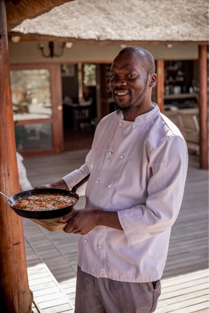 A man in a chef 's uniform is holding a pan of food.
