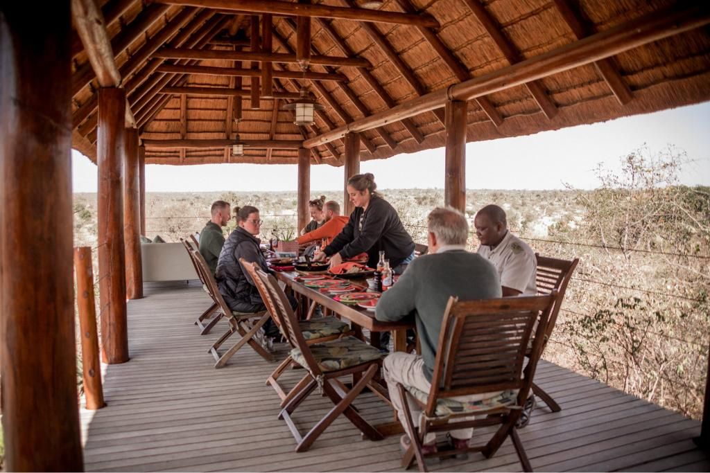 A group of people are sitting at a table under a thatched roof.