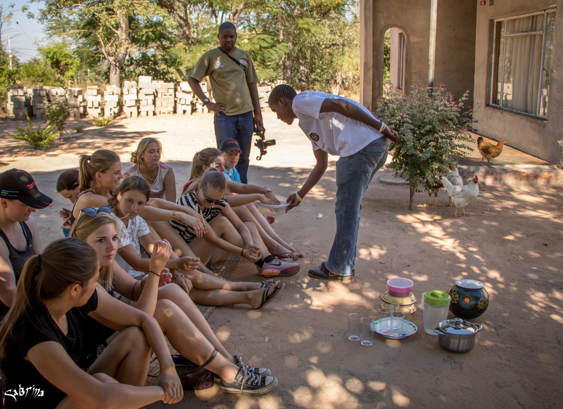 A group of people are sitting on the ground and a man is pointing at something.