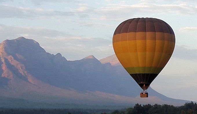 A hot air balloon is flying in the sky with mountains in the background.