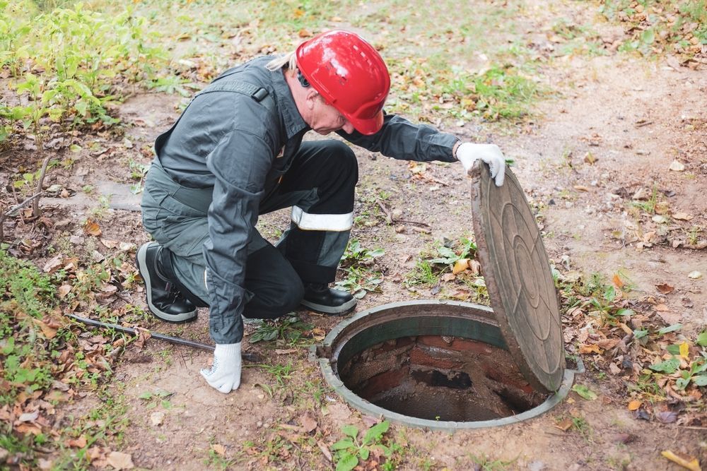 A man is kneeling down in front of a manhole cover.