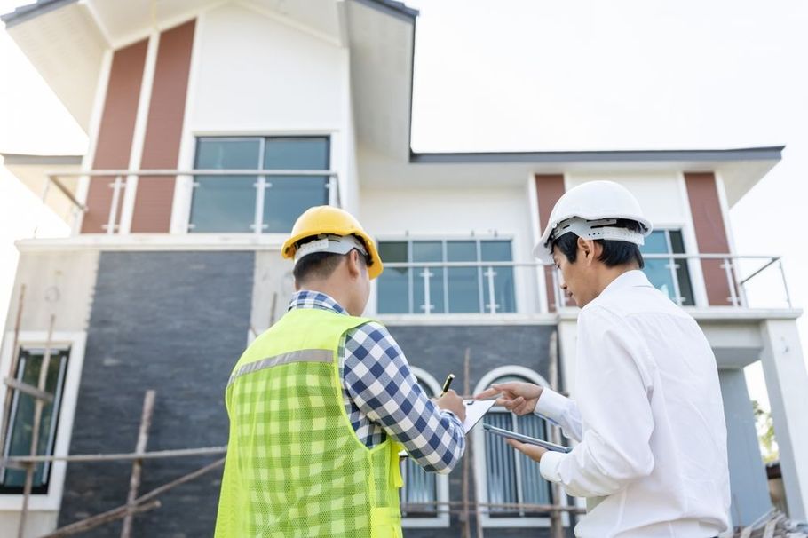 Two construction workers are standing in front of a house under construction.