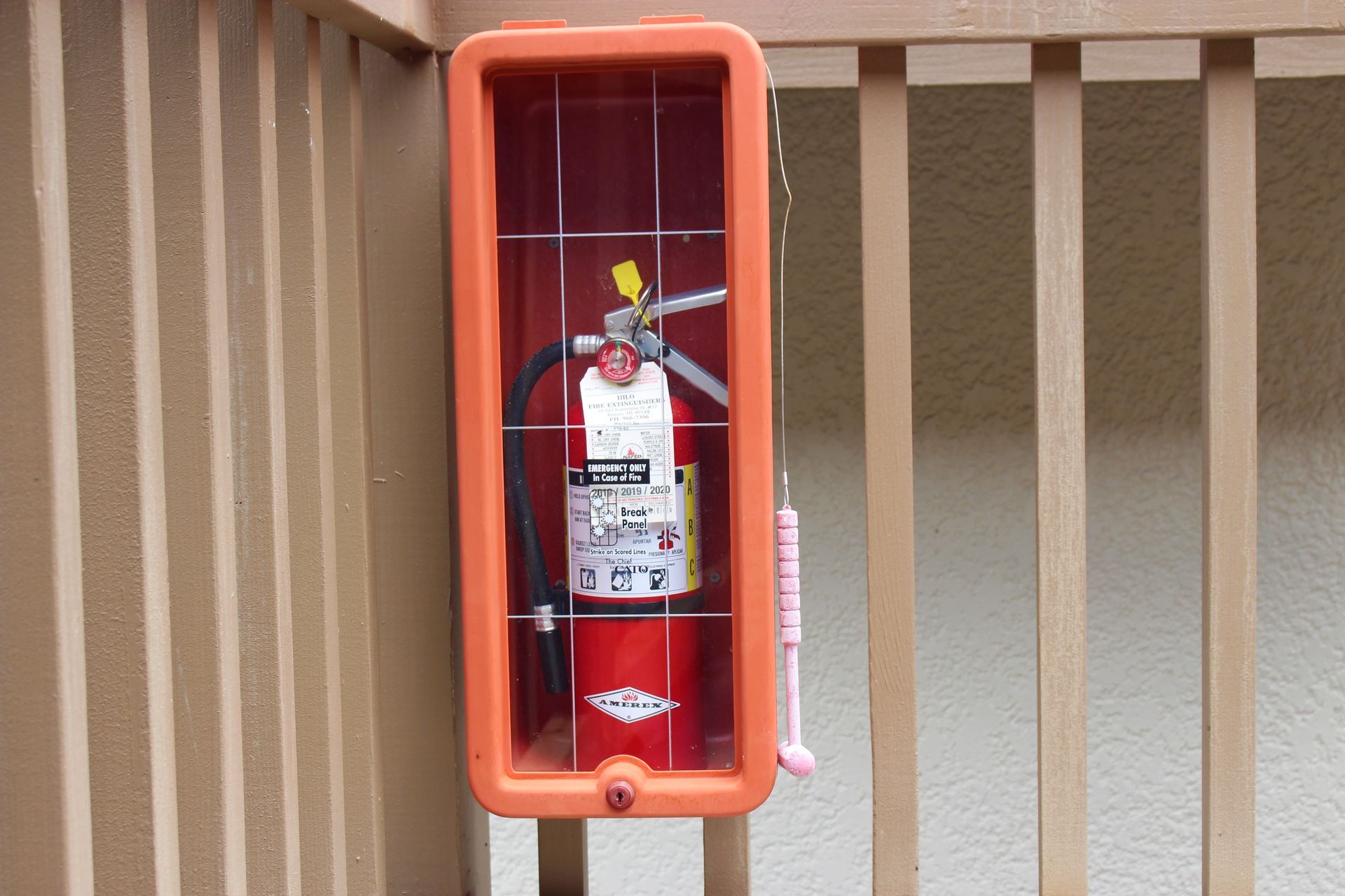 A red fire extinguisher is sitting in an orange box on the side of a building.