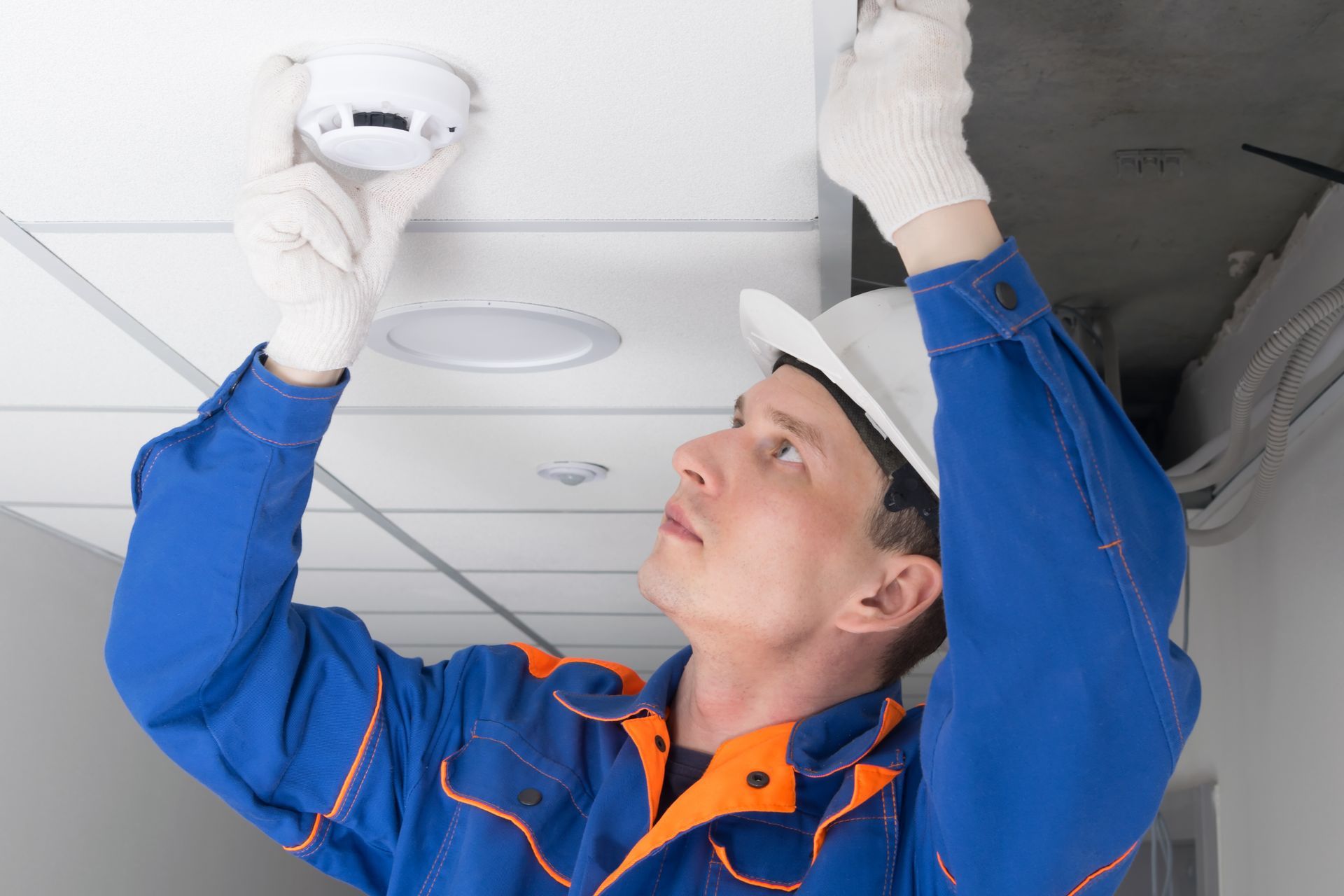 A man is installing a smoke detector on the ceiling.