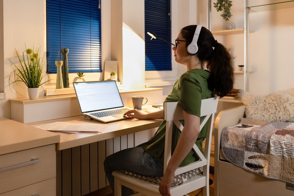 A woman is sitting at a desk with a laptop and headphones on.