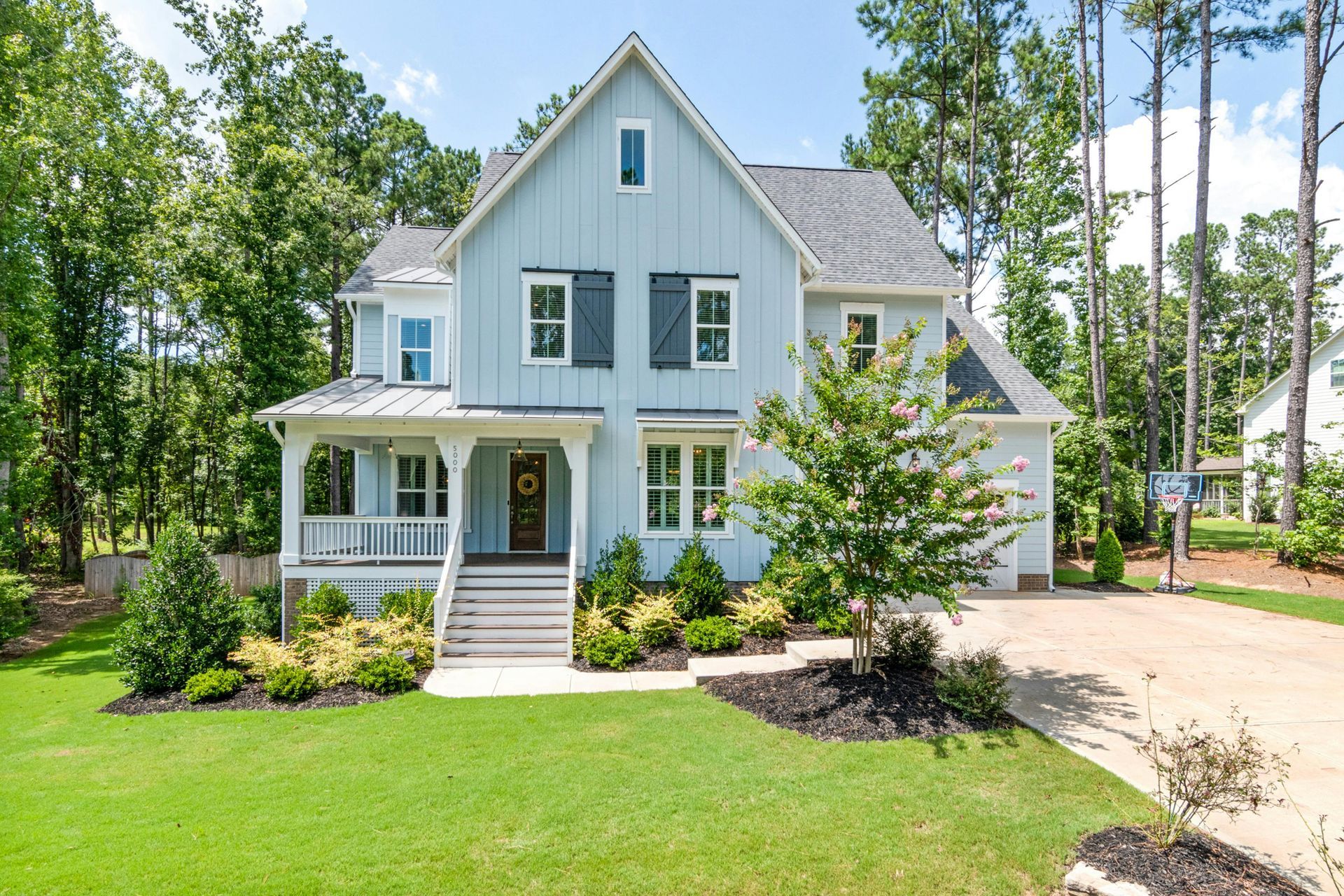 Light blue house with a porch and black shutters, set in a lush green yard.