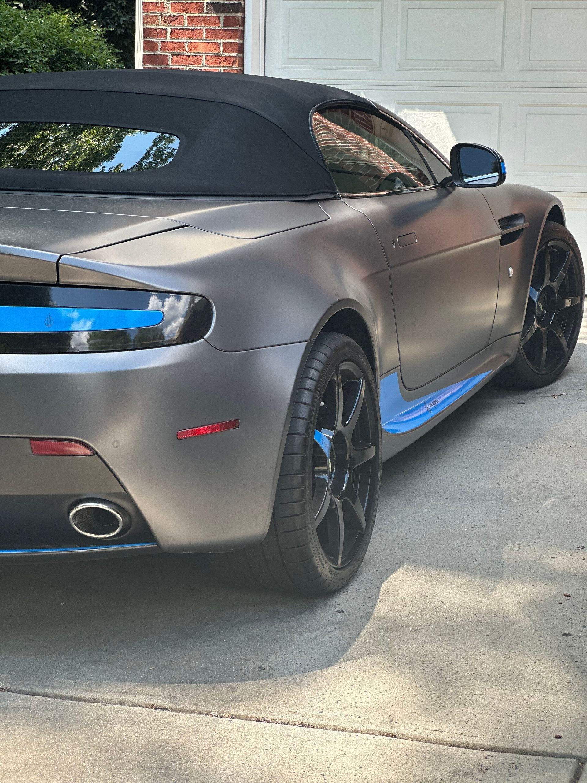 A silver sports car with a blue stripe on the side is parked in a driveway.