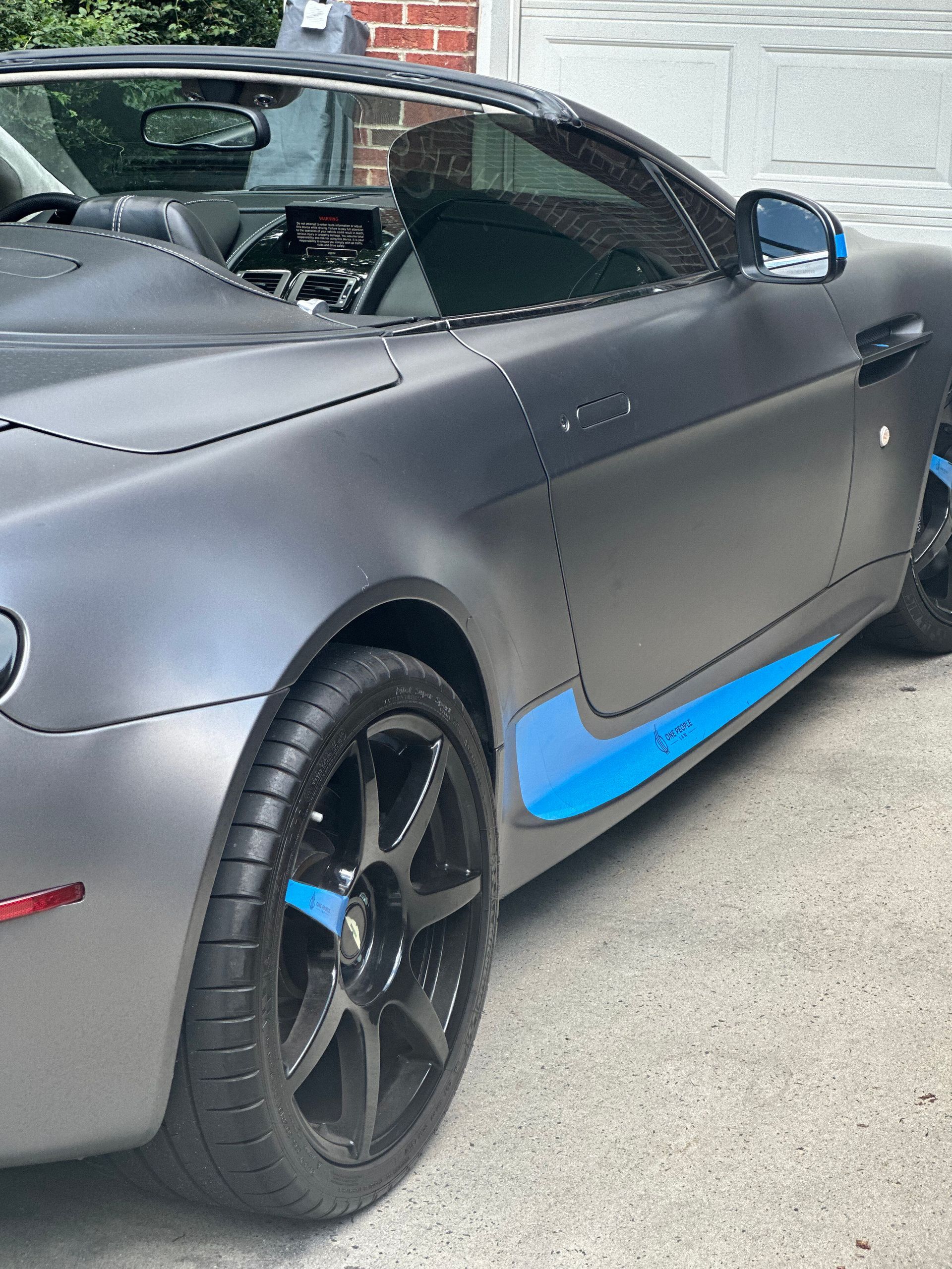 A gray sports car with a blue stripe on the side is parked in a driveway.