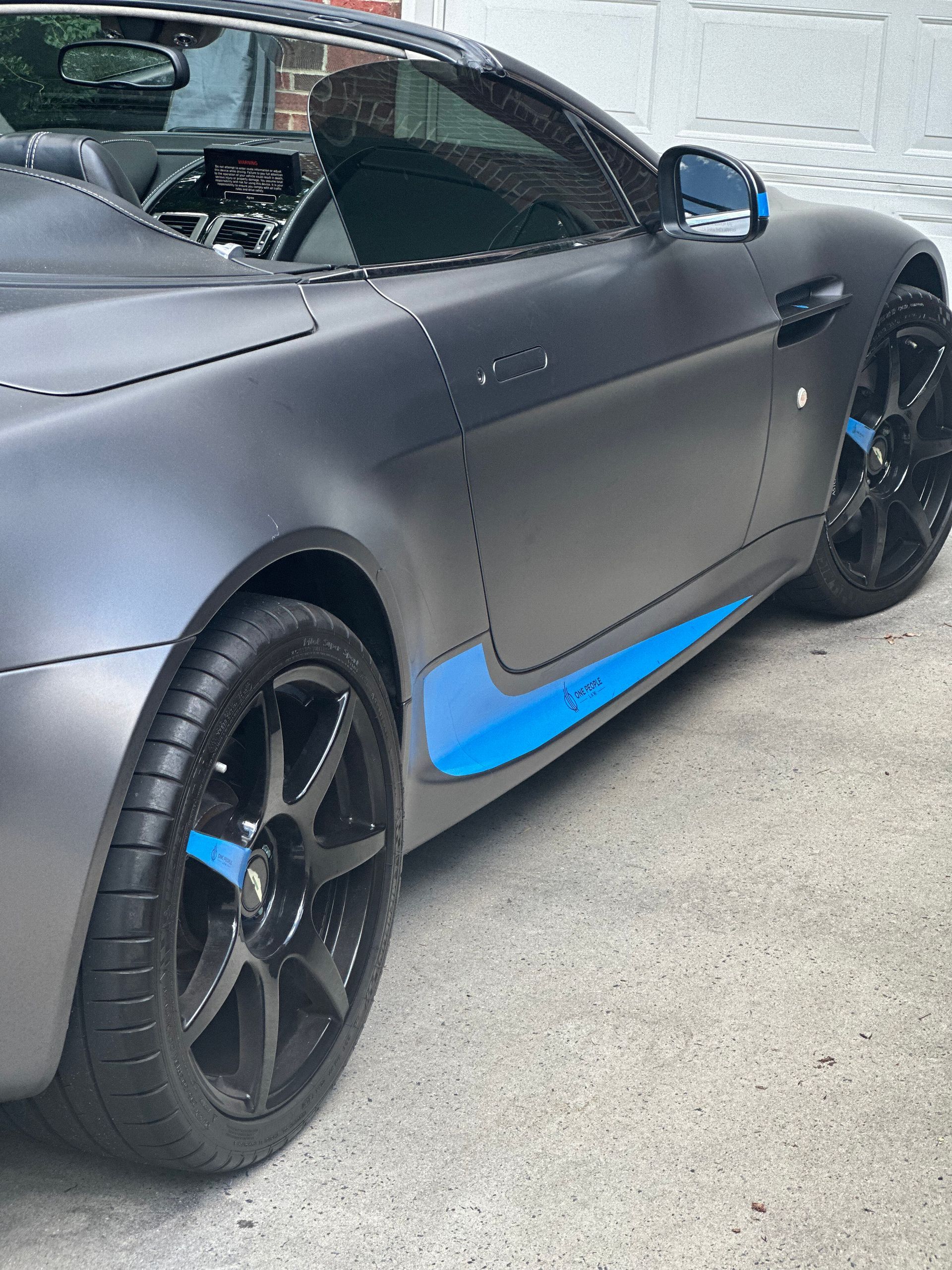 A gray sports car with a blue stripe on the side is parked on the side of the road.