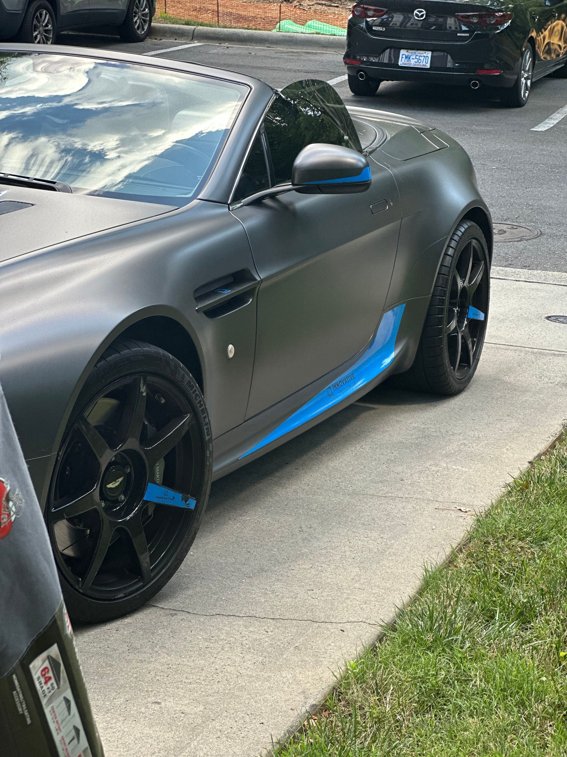 A black sports car with blue stripes on the side is parked on the side of the road.