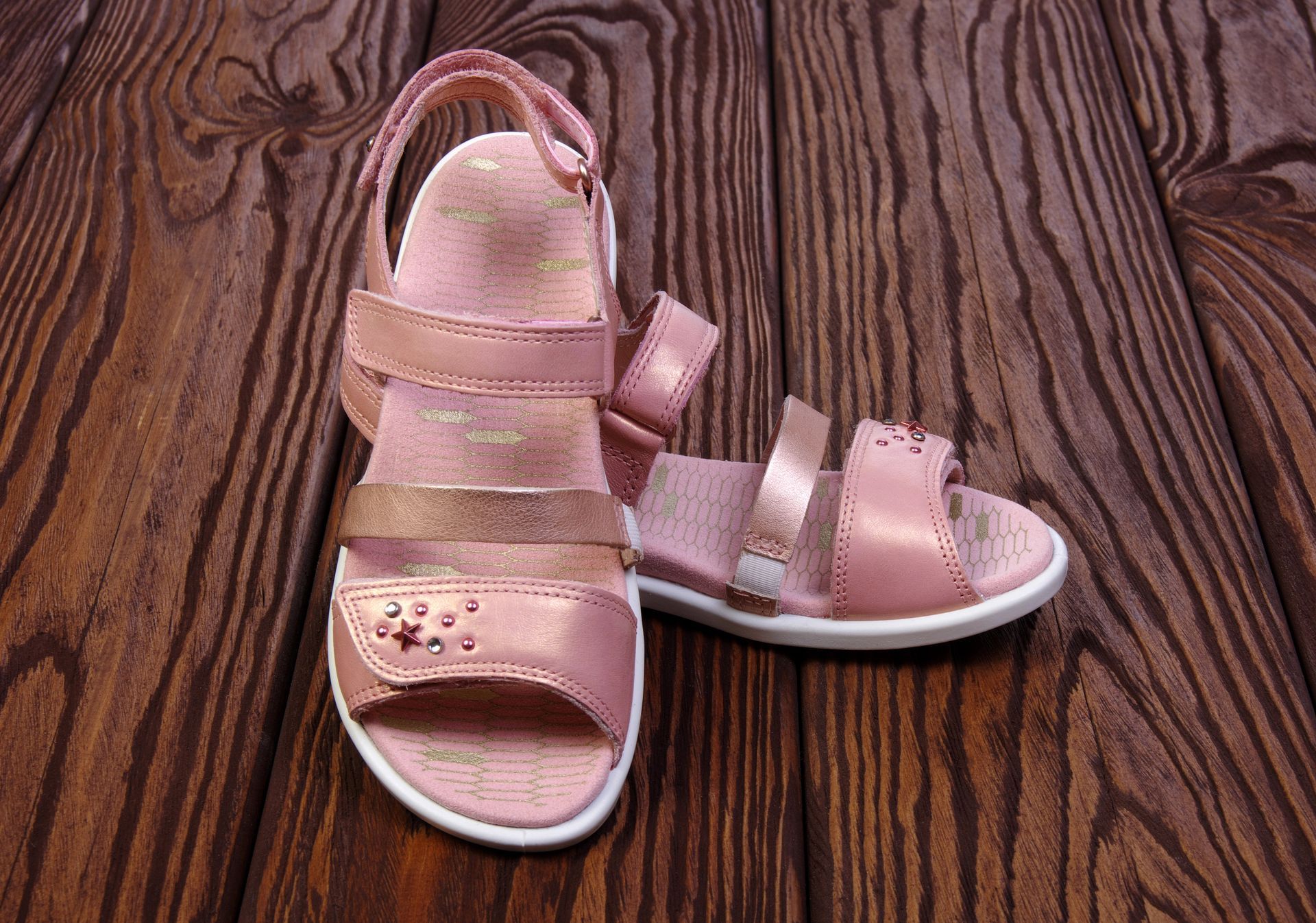 Sandali rosa per bambini su una superficie di legno scuro.