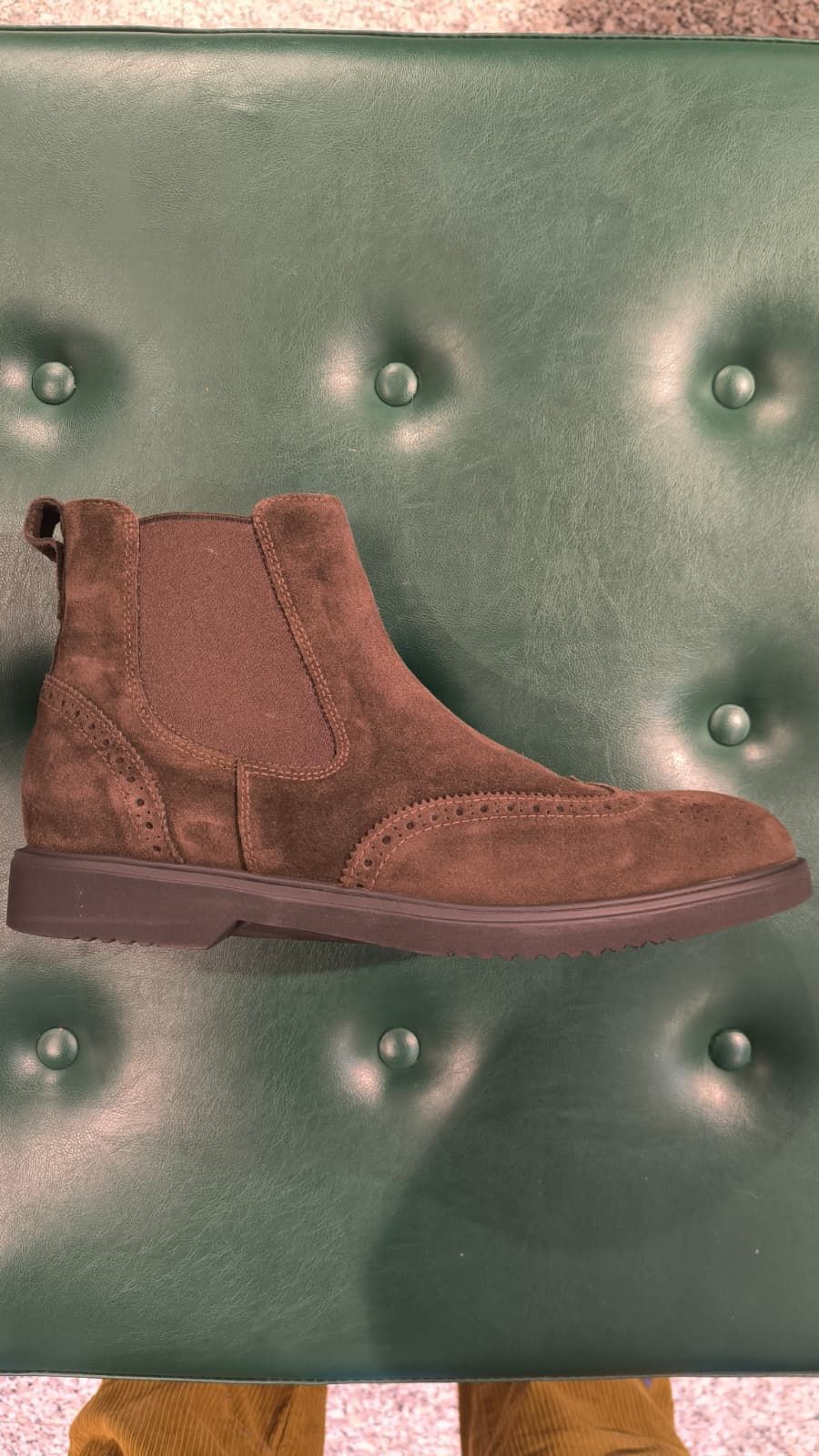 Piede di una persona con una scarpa scamosciata marrone su una scatola da scarpe. Pantaloni beige arrotolati