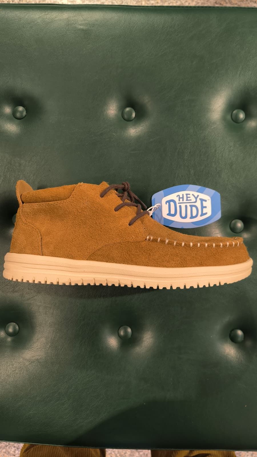 Stivaletto Chelsea in pelle scamosciata nera su una superficie verde, con una scatola grigia dietro.