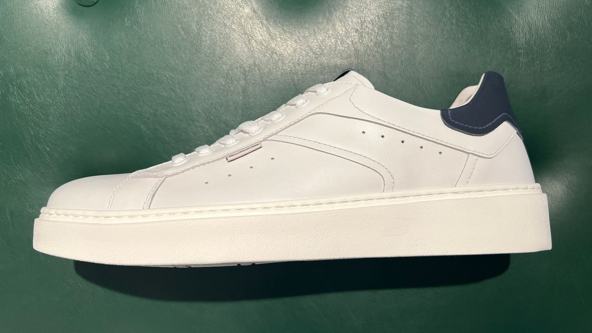 Persona che tiene in mano una scarpa da corsa Nike Air Max bianca e nera su una strada lastricata.