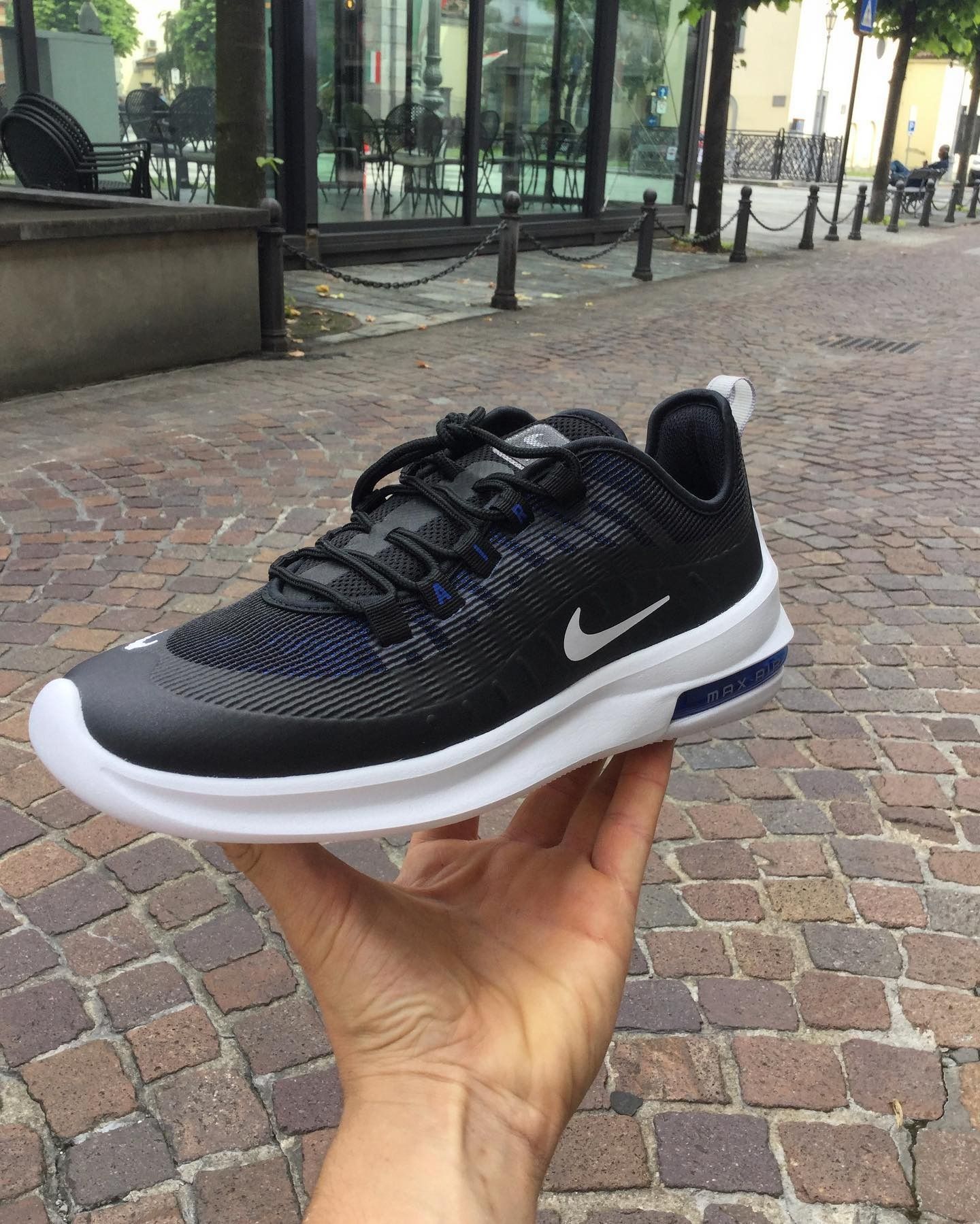 Persona che tiene in mano una scarpa da corsa Nike Air Max bianca e nera su una strada lastricata.