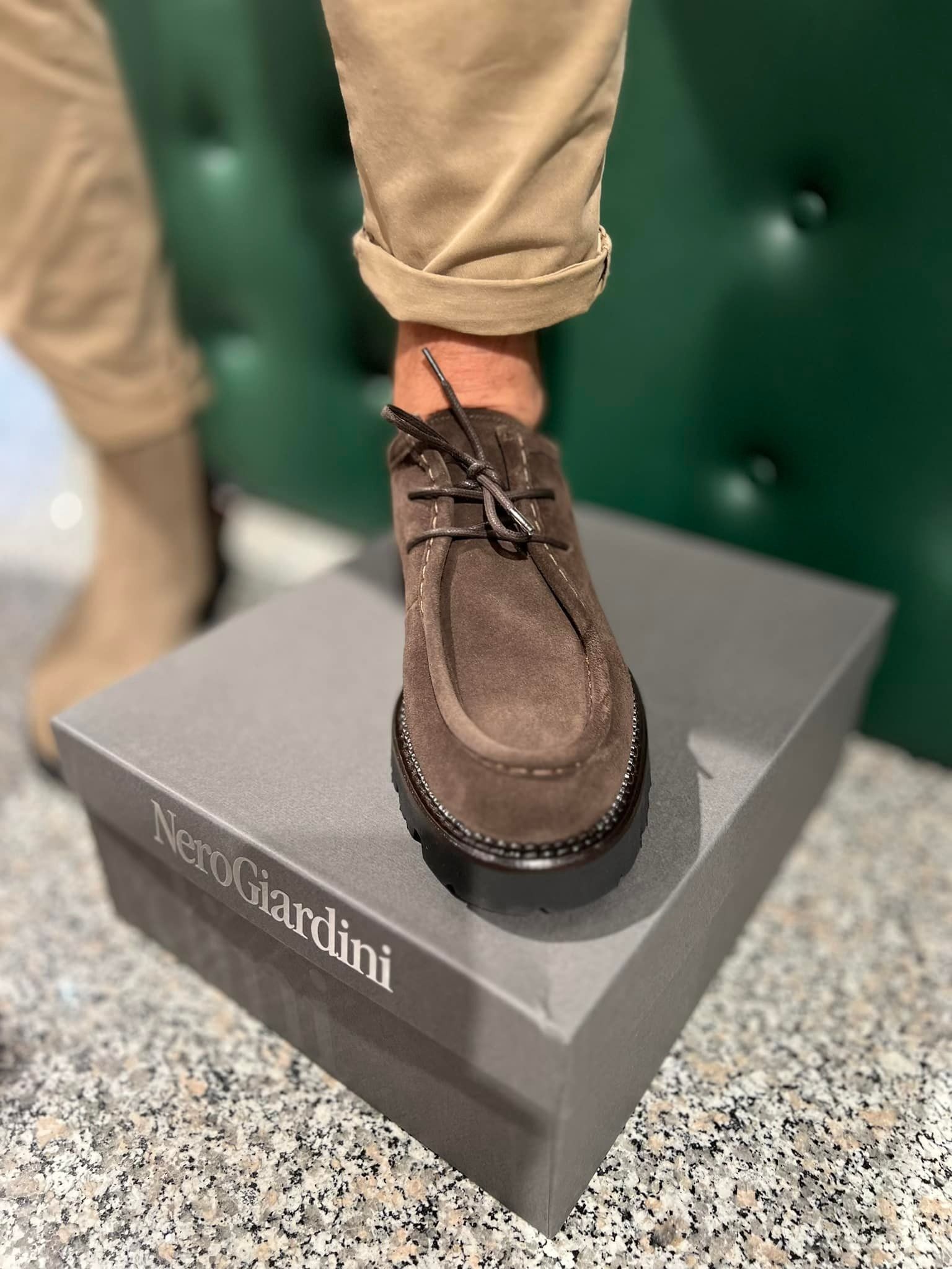 Piede di una persona con una scarpa scamosciata marrone su una scatola da scarpe. Pantaloni beige arrotolati