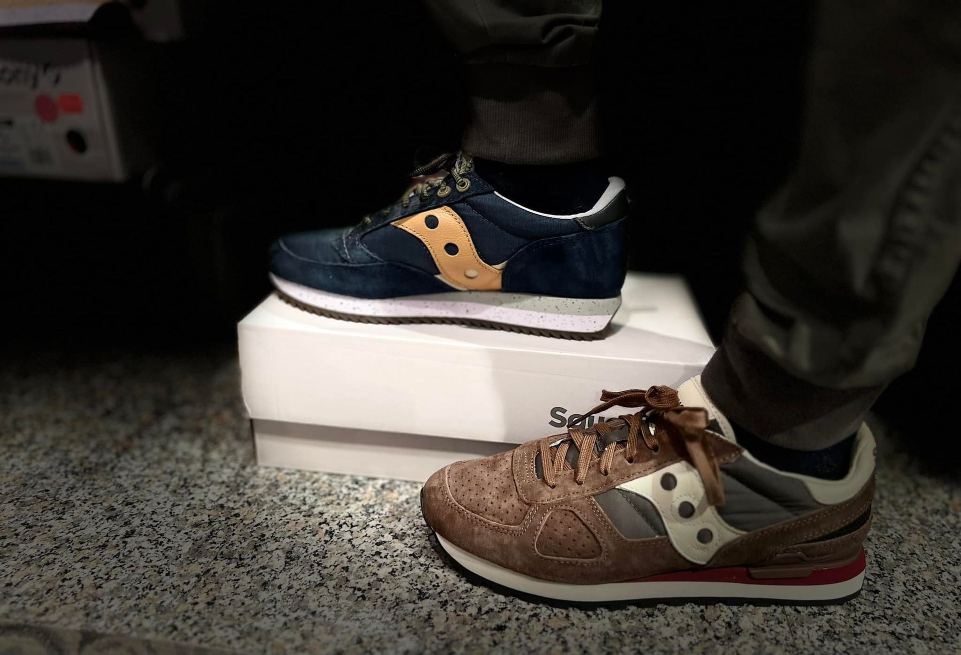 Due scarpe da ginnastica Saucony, una blu e una marrone, esposte e indossate da qualcuno.