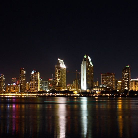 a city skyline at night with a large body of water in the foreground