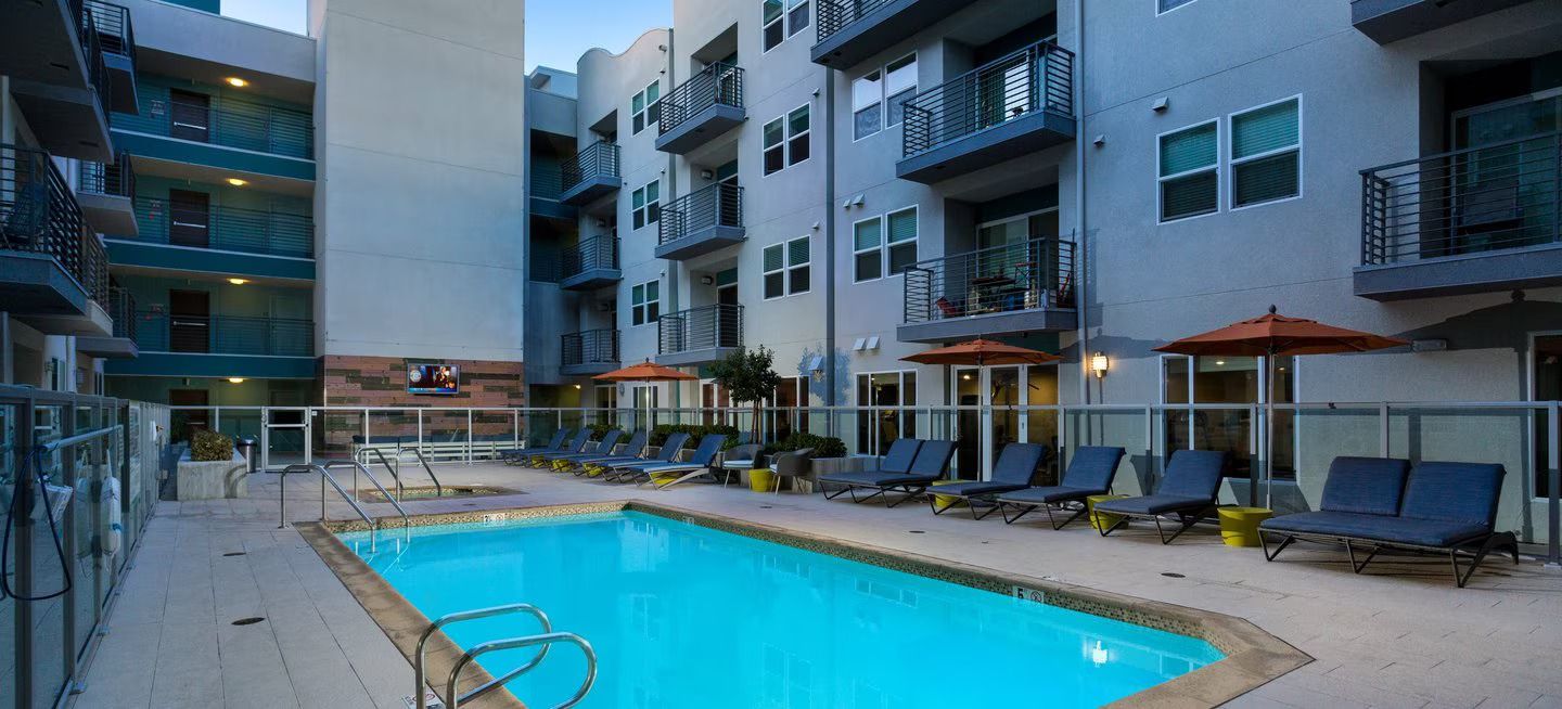 a large swimming pool surrounded by chairs and umbrellas in front of a building .