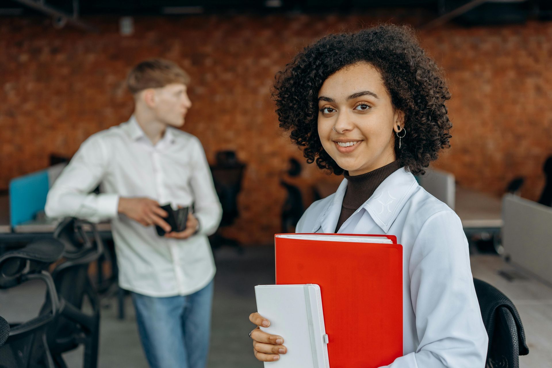 A woman is holding a red folder in front of a man in an office.