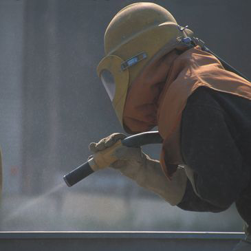 A man wearing a helmet and gloves is sandblasting