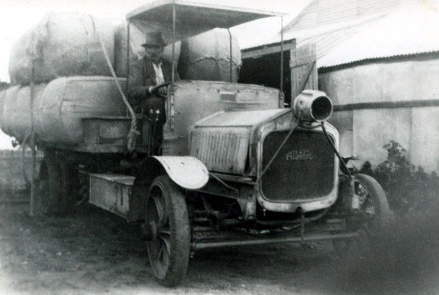 A black and white photo of an old truck with a man in the driver 's seat