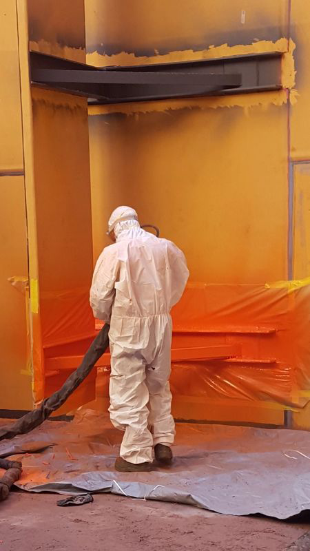 A man in a protective suit is spray painting a wall.