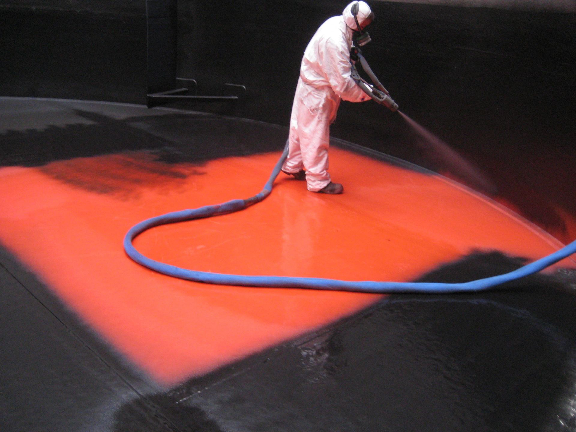 A man in a white suit is spraying red paint on a black surface