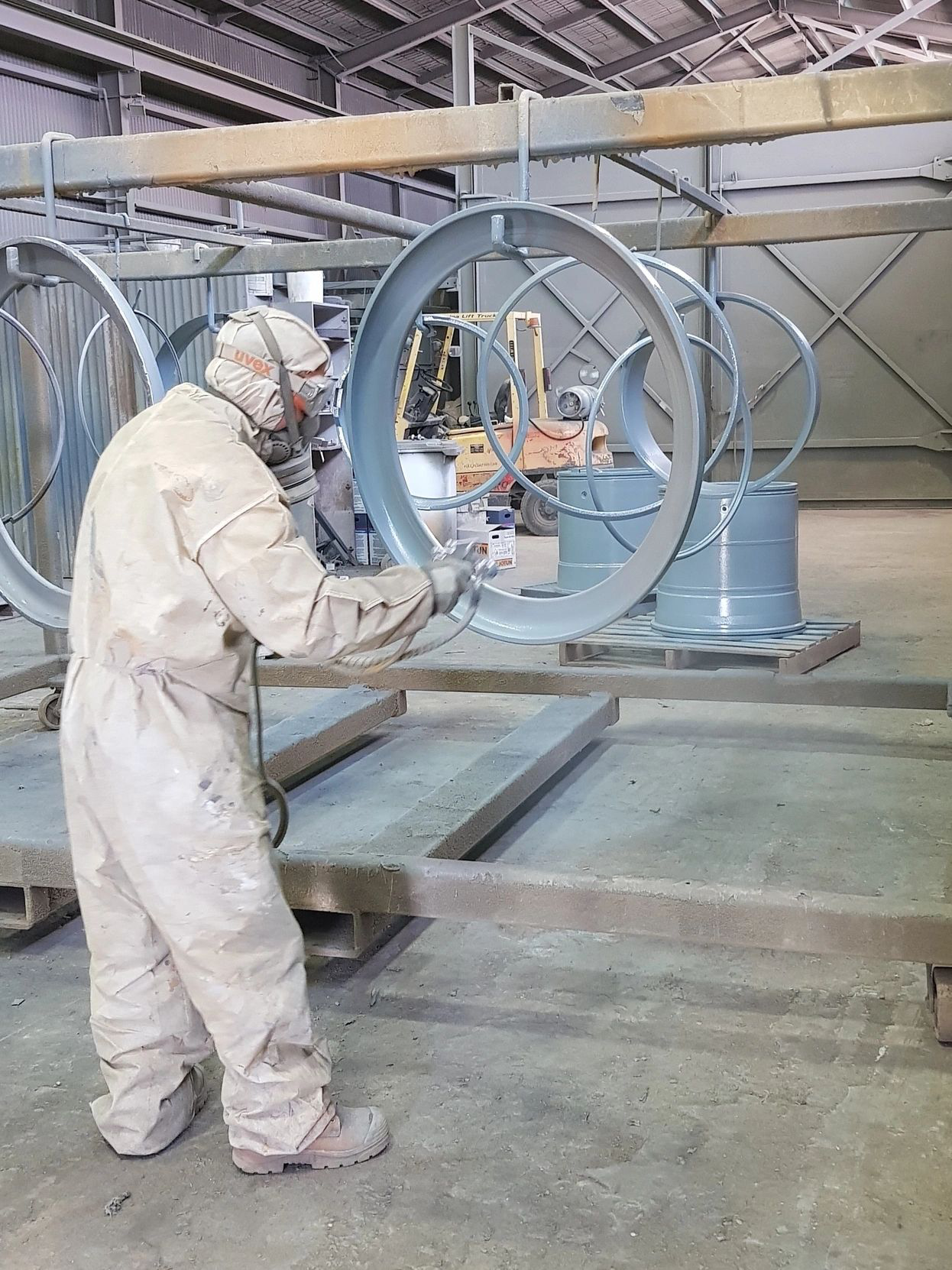 A man in a white coveralls is painting a metal object in a factory.