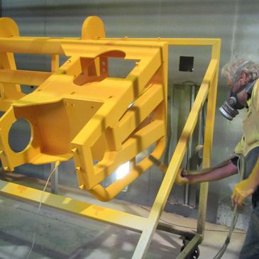 A man wearing a gas mask is painting a yellow object