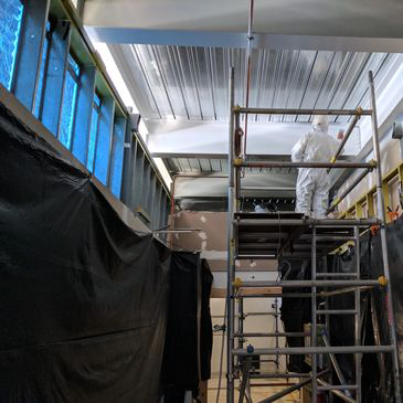 A man in a white suit is standing on a scaffolding in a room.