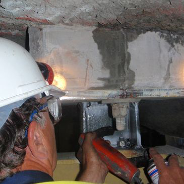 A man wearing a hard hat and goggles is working on a piece of metal.