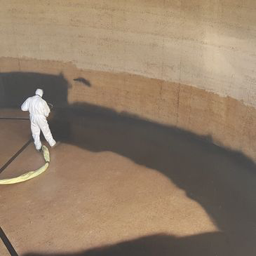 A man in a white suit is spraying a wall with a hose.