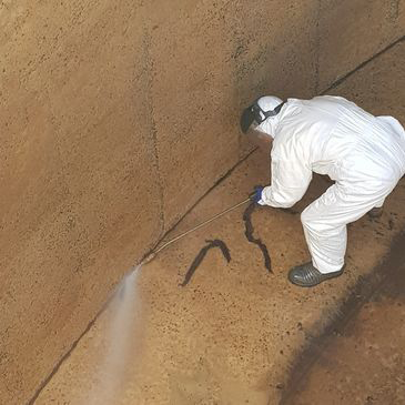 A man in a white suit is spraying water on a wall.