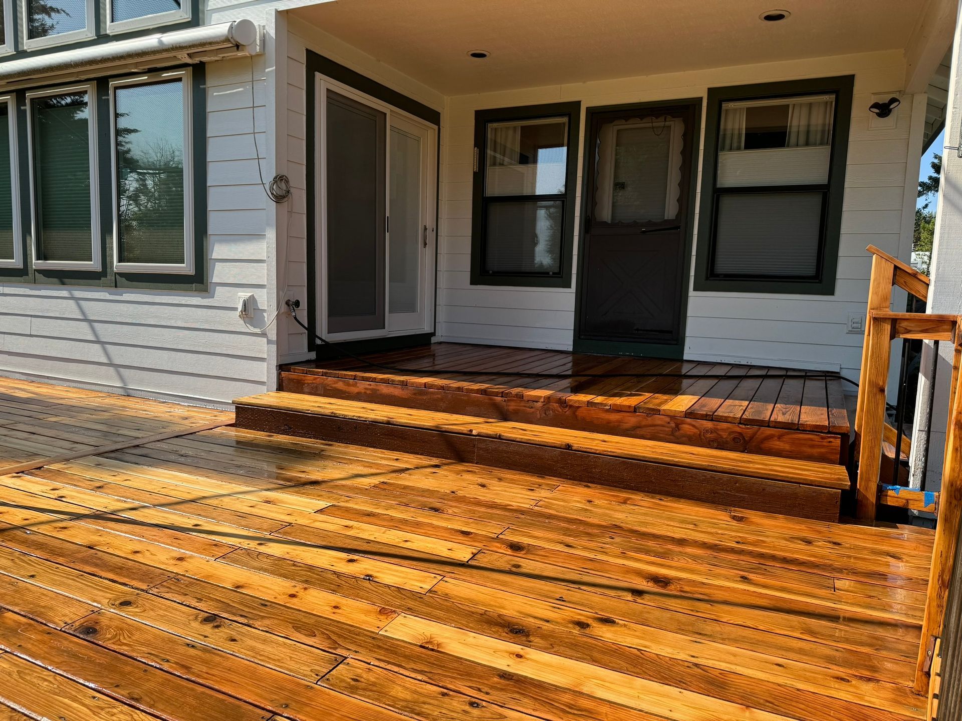 A wooden deck with stairs leading up to the front door of a house.