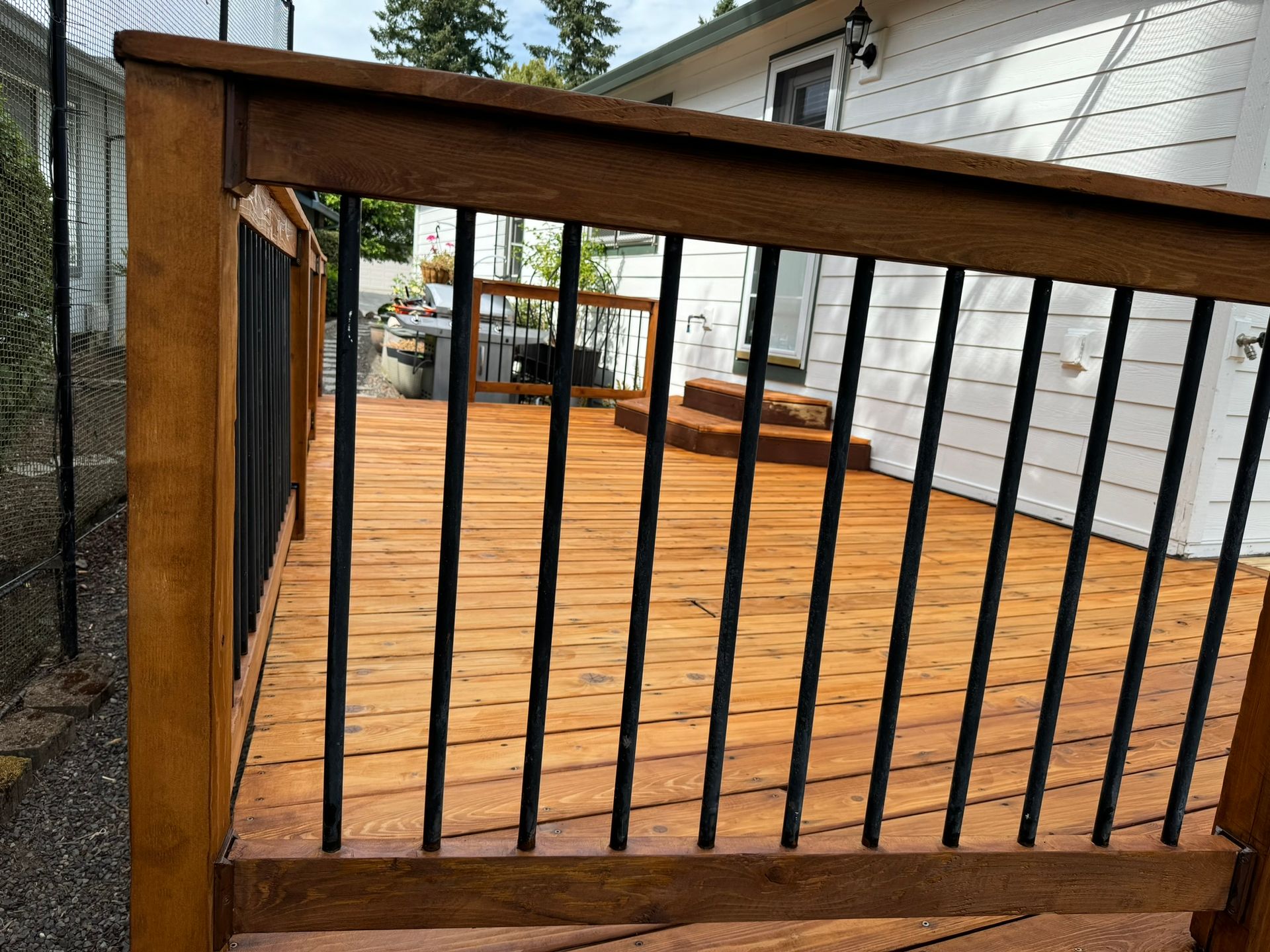 A wooden deck with a metal railing and stairs in front of a house.