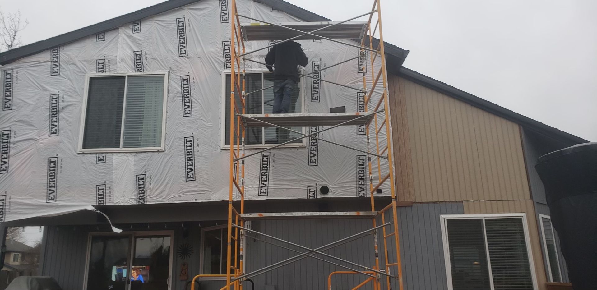 A man is standing on a scaffolding in front of a house.