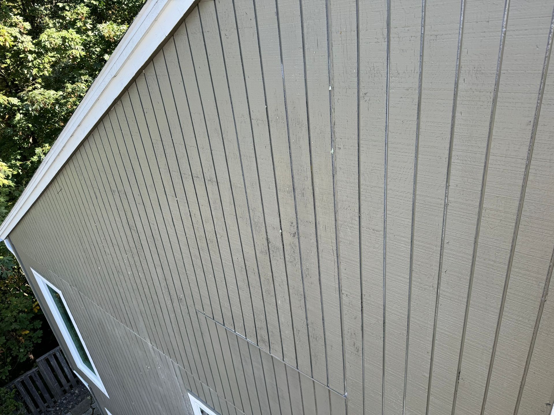 The side of a house with a fence and trees in the background.