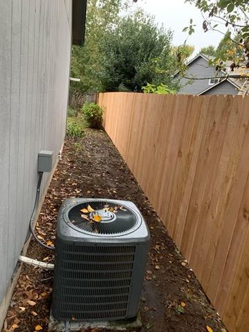 An air conditioner is sitting on the side of a house next to a wooden fence.