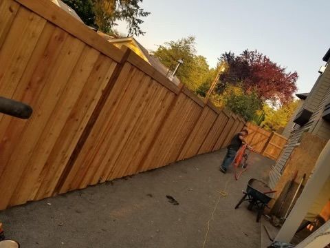 A man is standing next to a wooden fence in a driveway.