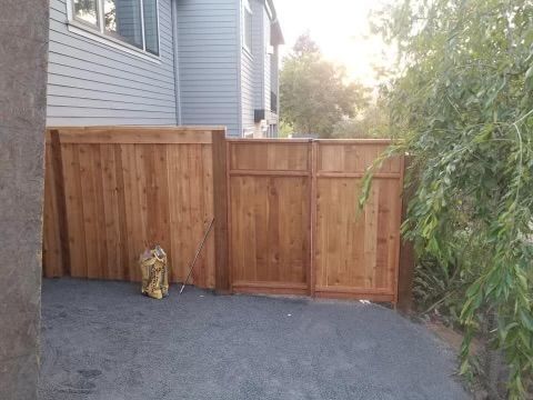 A wooden fence surrounds a driveway in front of a house.