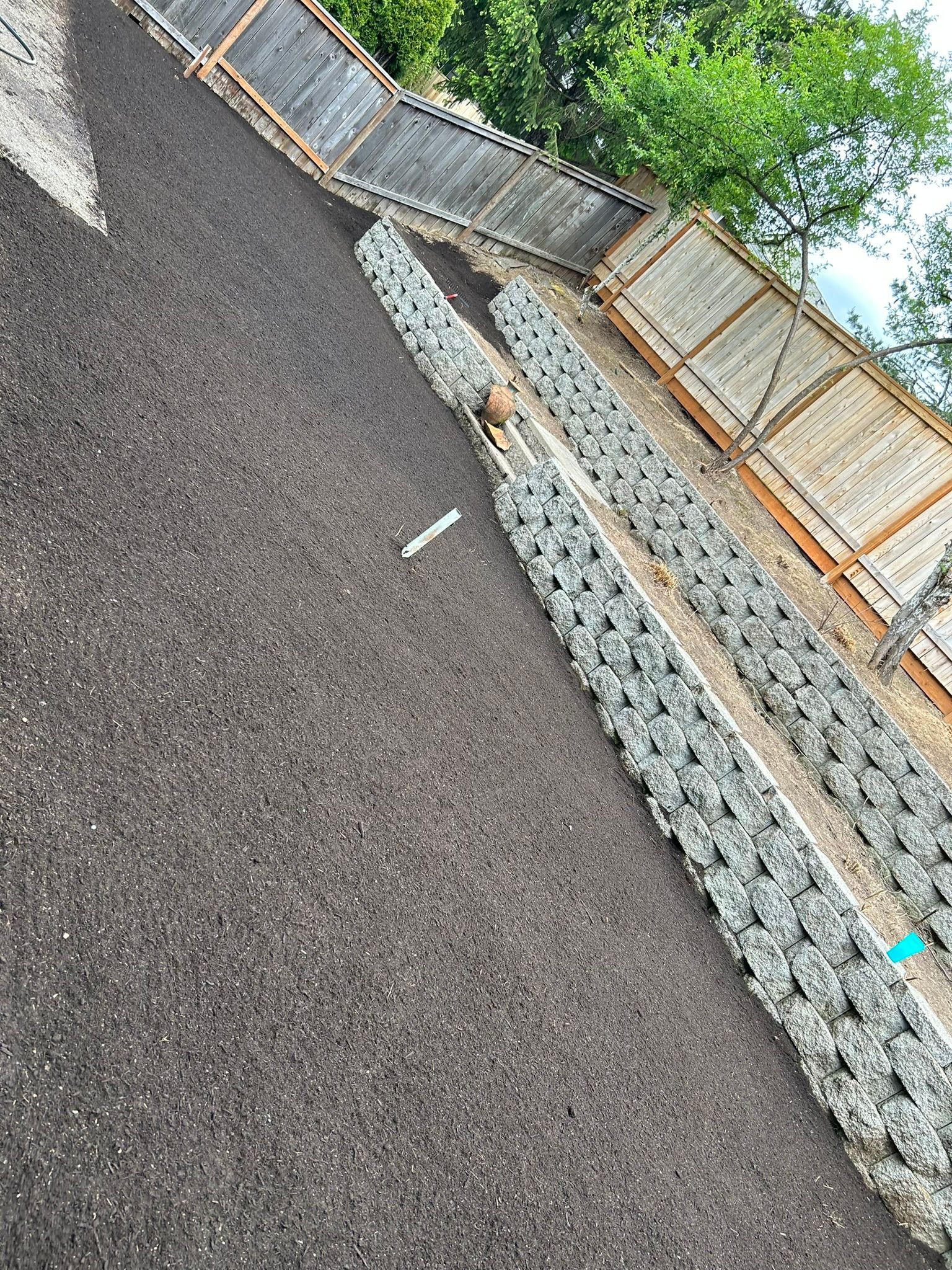 A pile of gravel is sitting on top of a dirt hill next to a wooden fence.