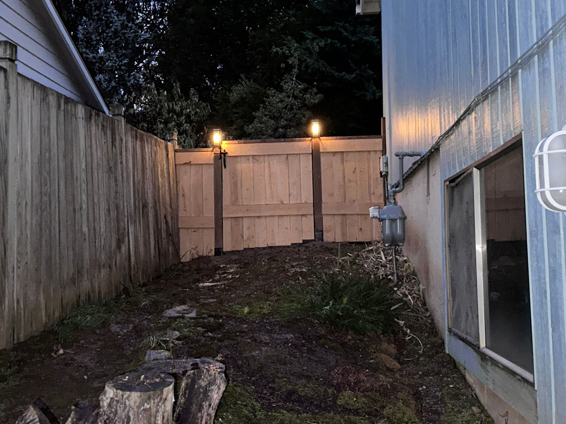 The backyard of a house with a wooden fence and lights.