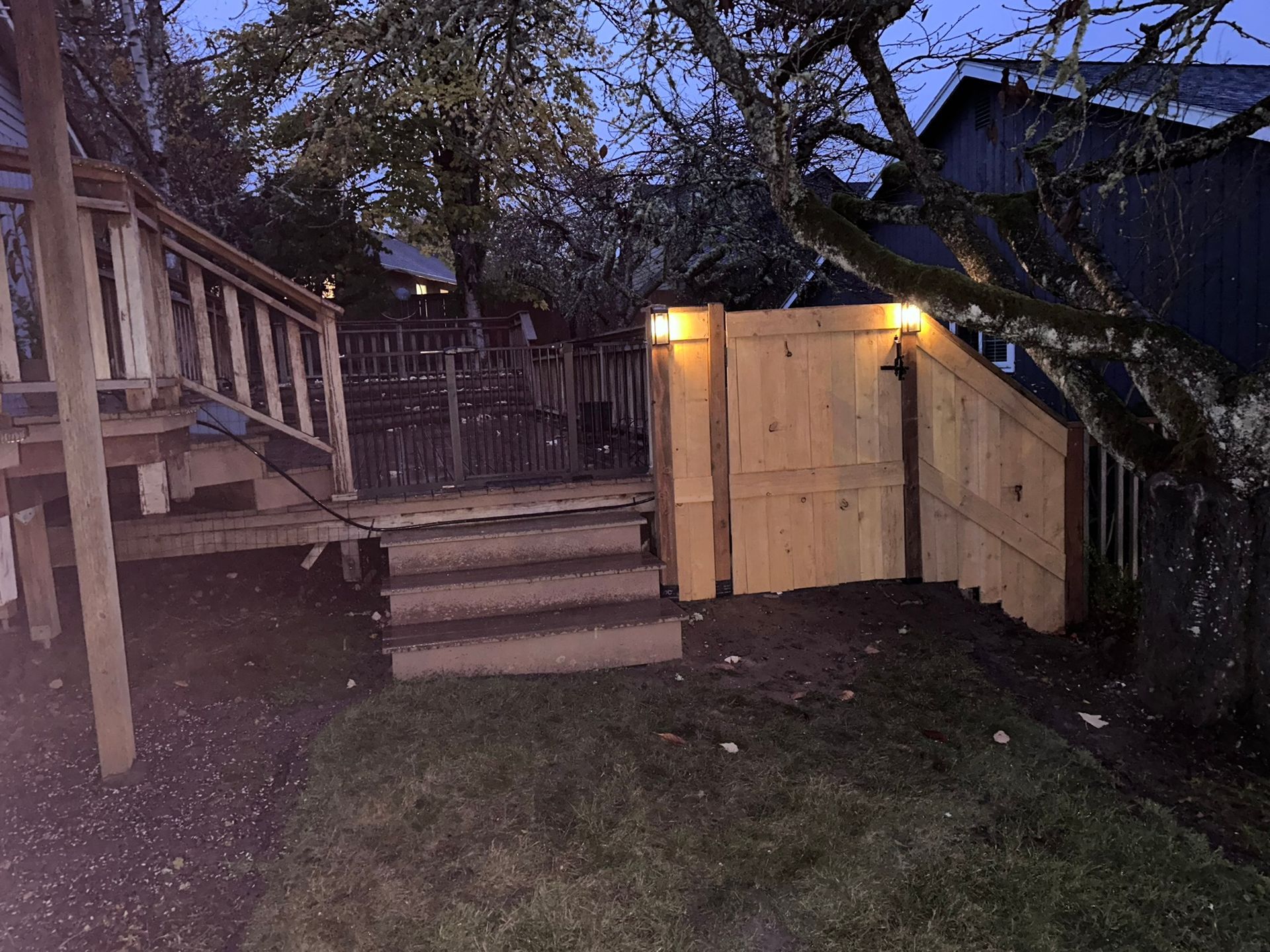 A wooden deck with stairs and a gate in the backyard at night.