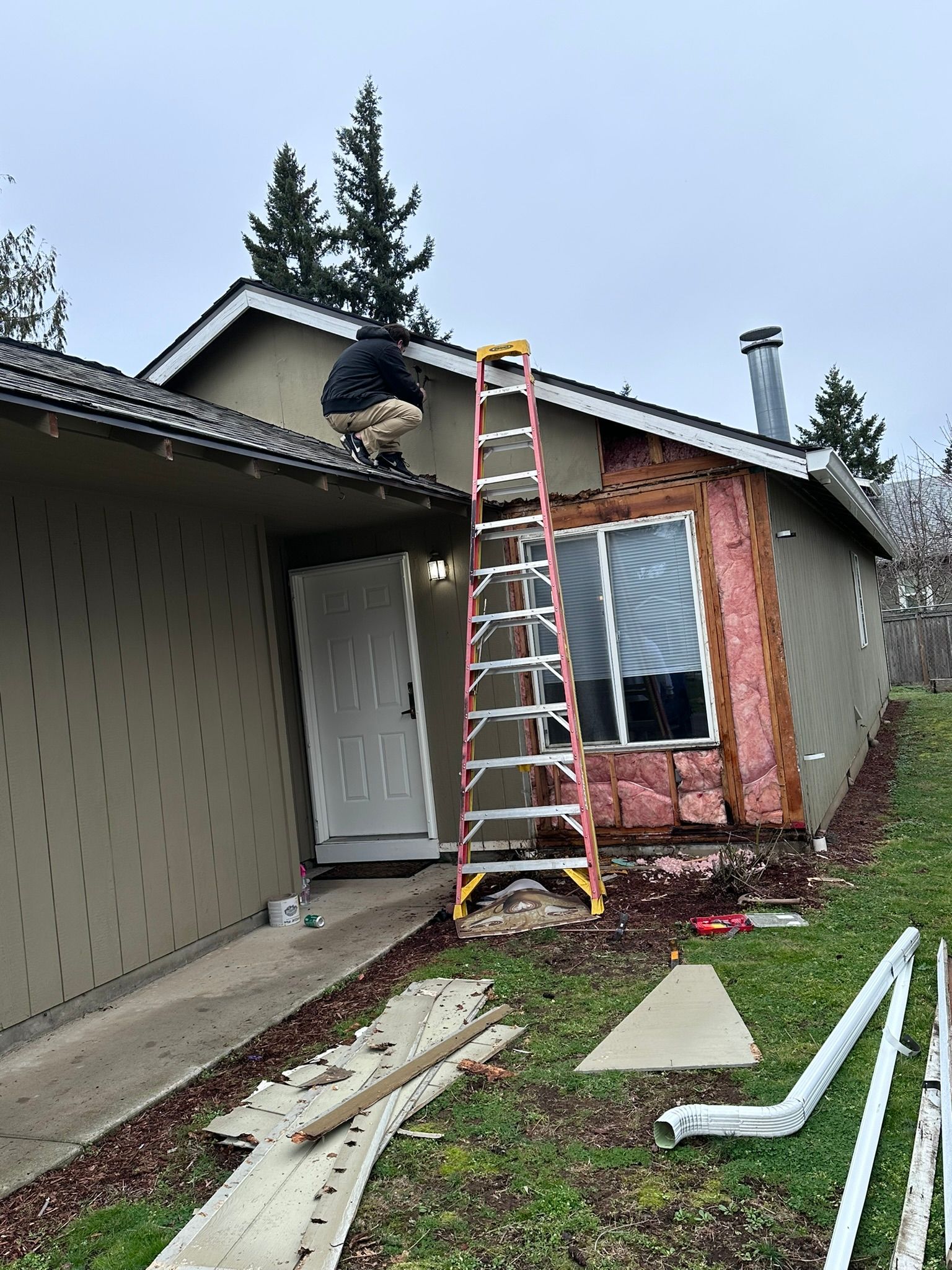 A man is sitting on the roof of a house next to a ladder.