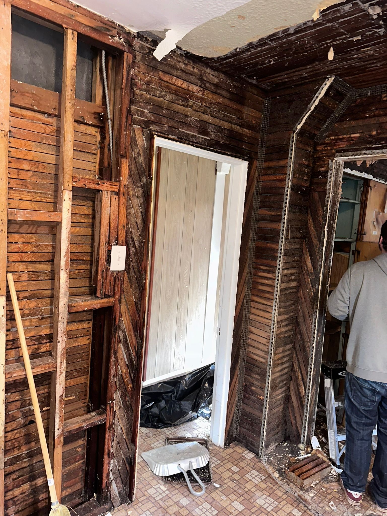 A man is standing in a room with wooden walls and a door.