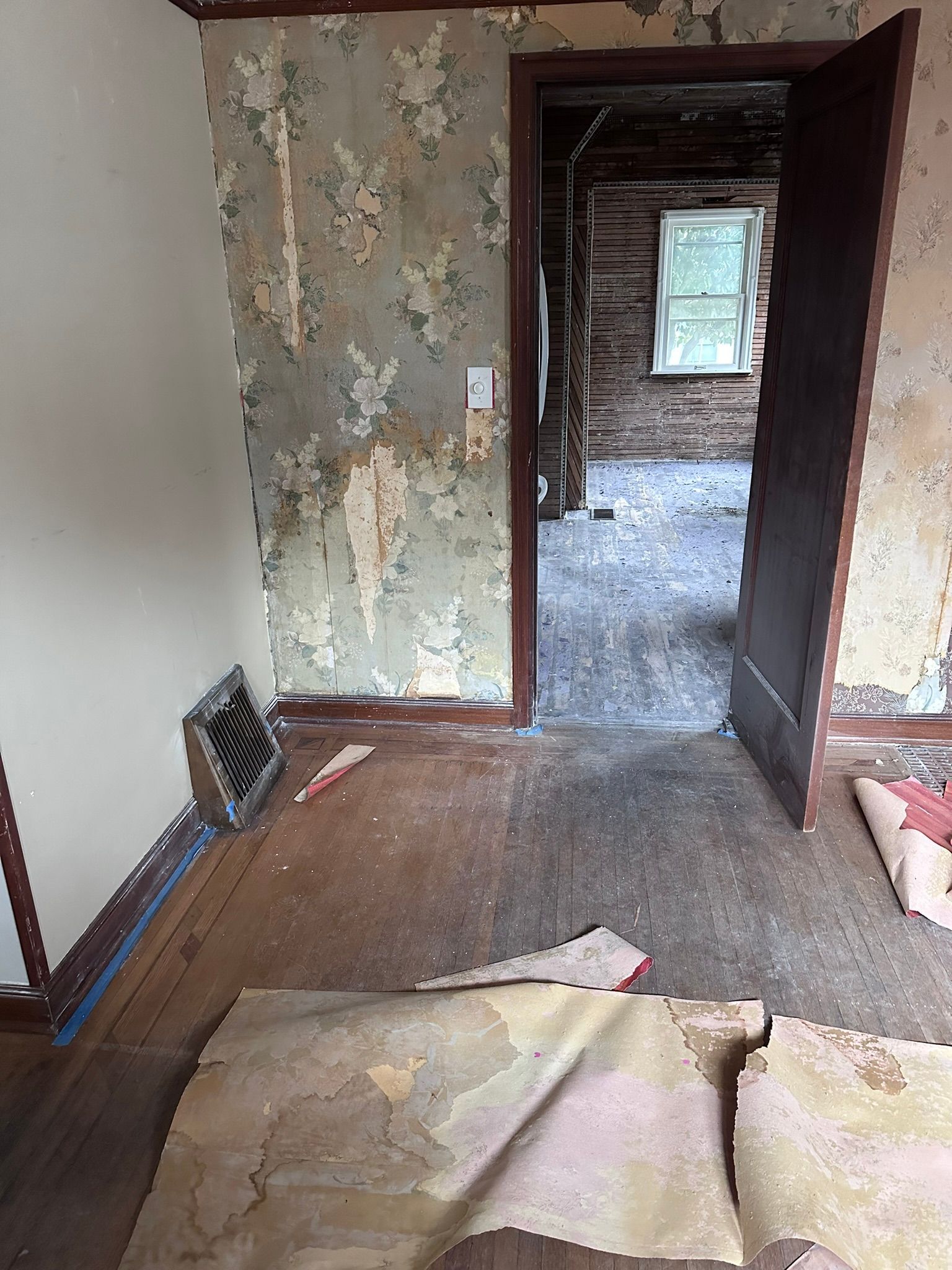 A room with peeling wallpaper and a doorway leading to another room.
